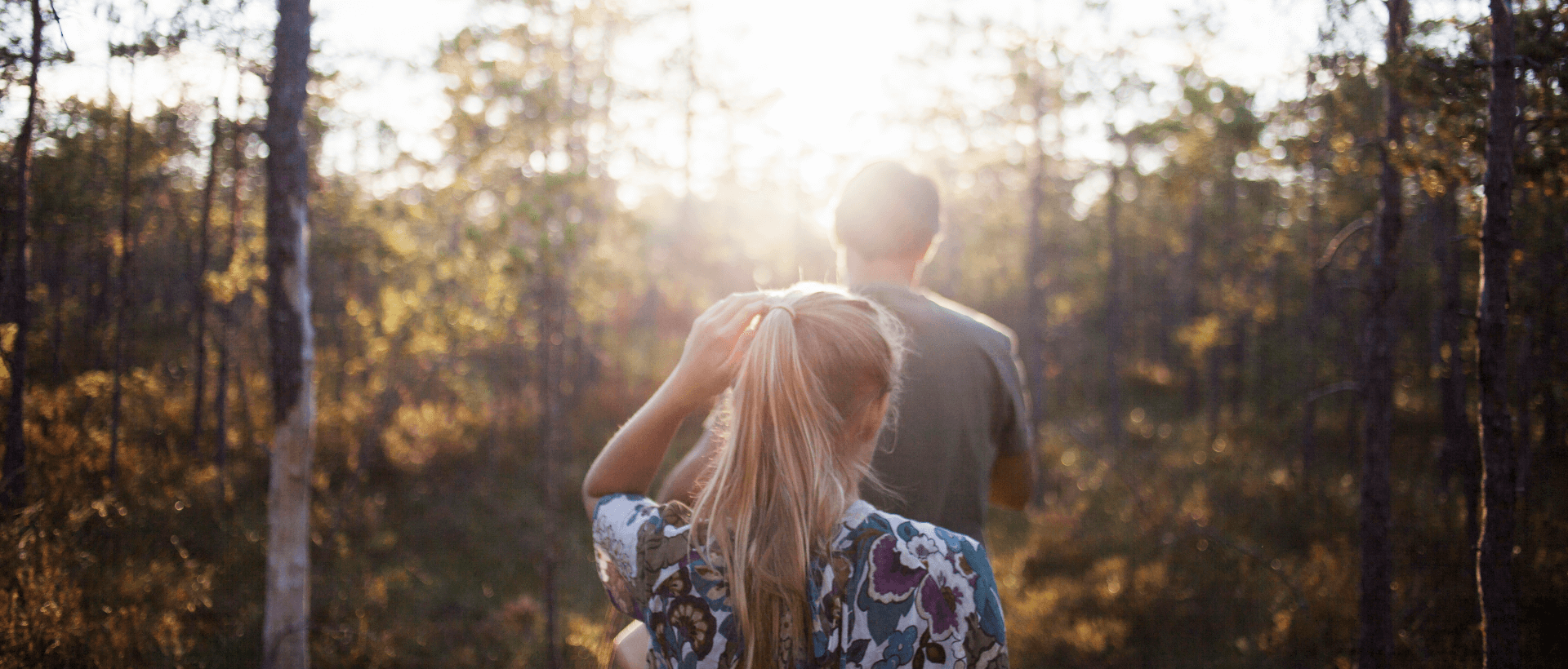 A young woman following a young man into the forest, summery atmosphere and sunshine, rear view